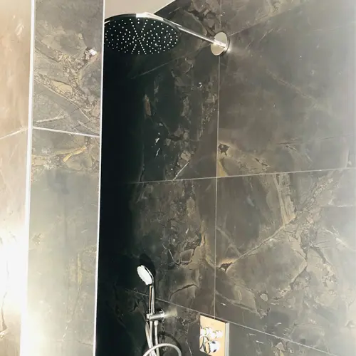 Douche avec carrelage foncé et pommeau mural réalisée par BH Plomberie